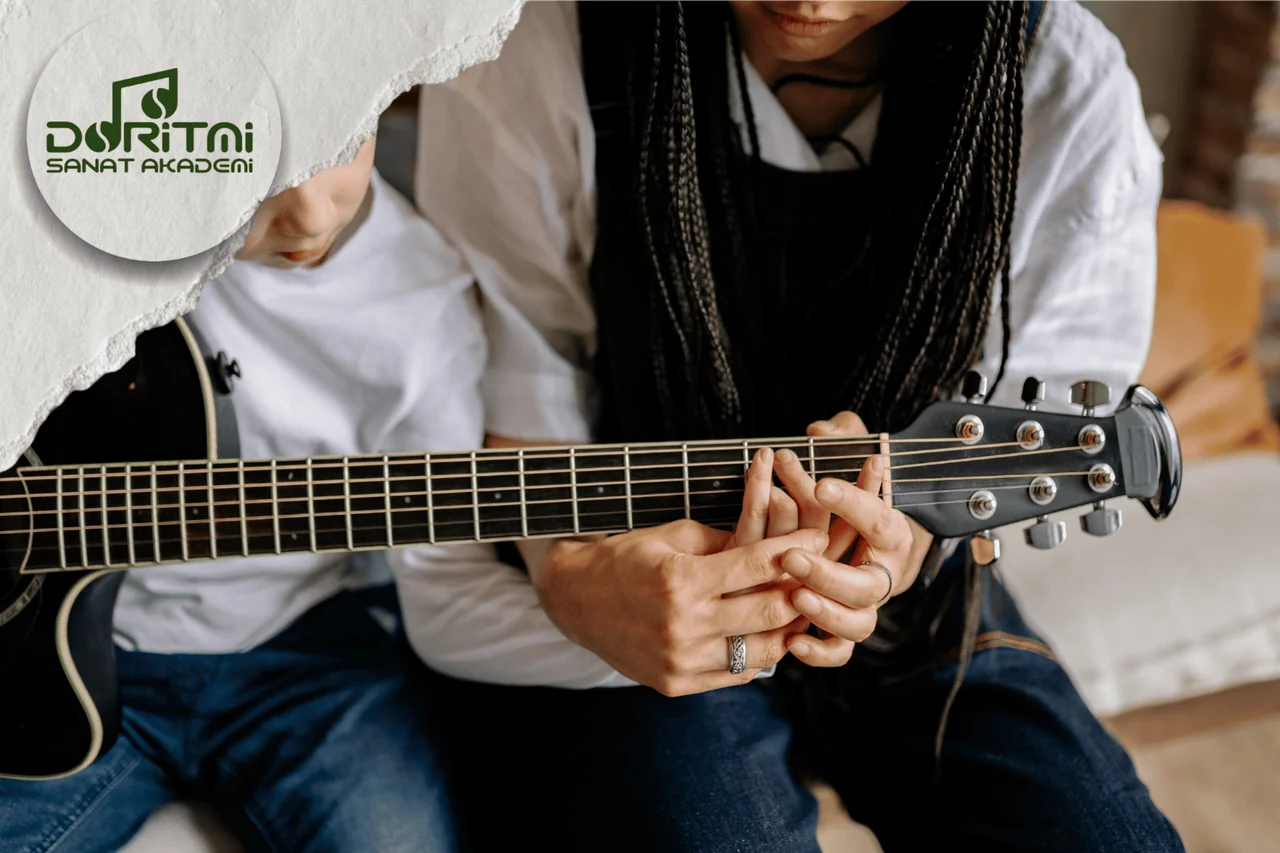 Siyah akustik gitarın sapında parmak konumunu çalışan iki kişi.