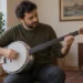 Alüminyum gövdeli ve perdesiz saplı standart cümbüşü mızrapla çalan yetişkin.