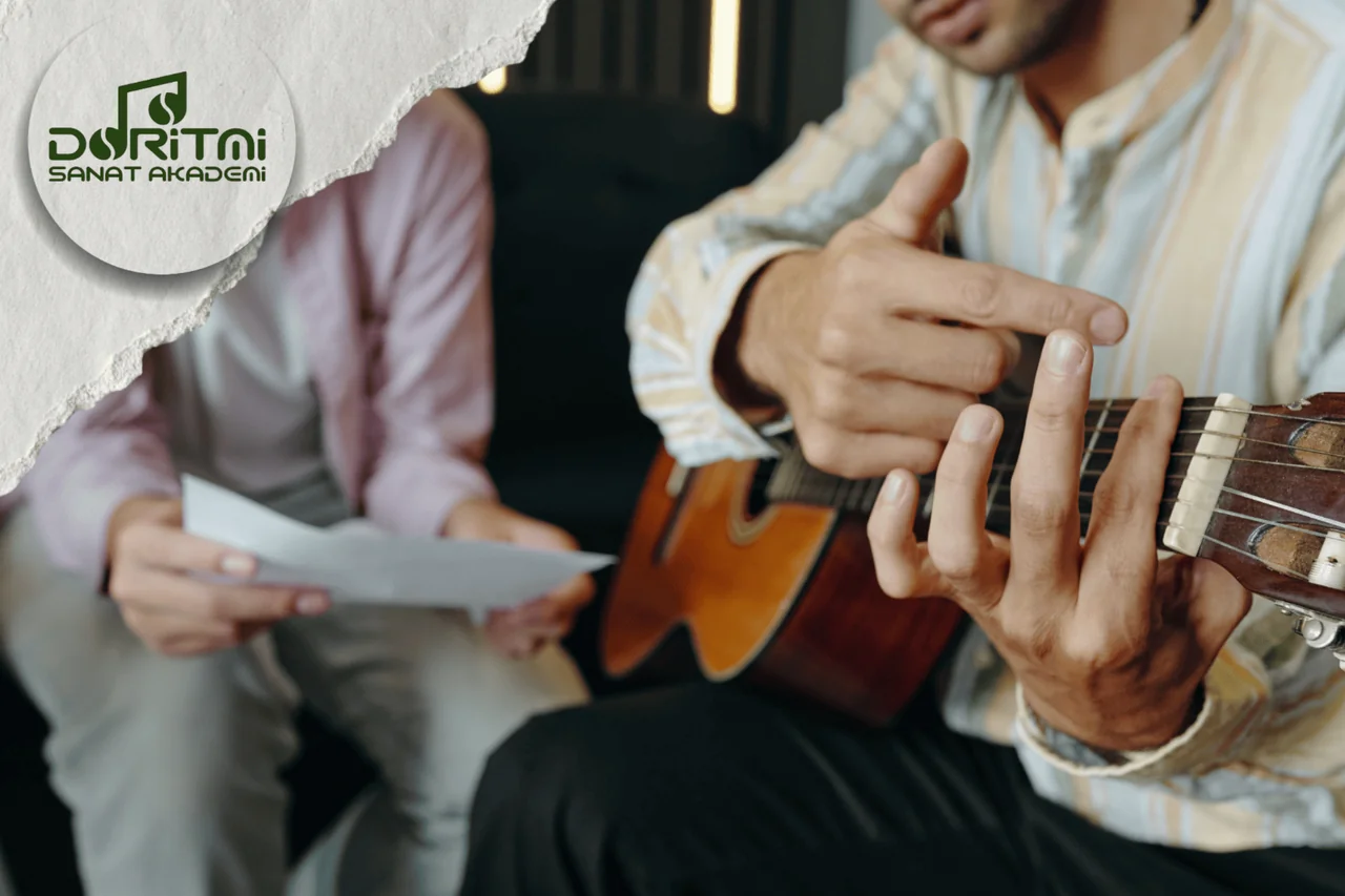 Gitar sapındaki parmak yerleşimini birlikte inceleyen iki kişi.